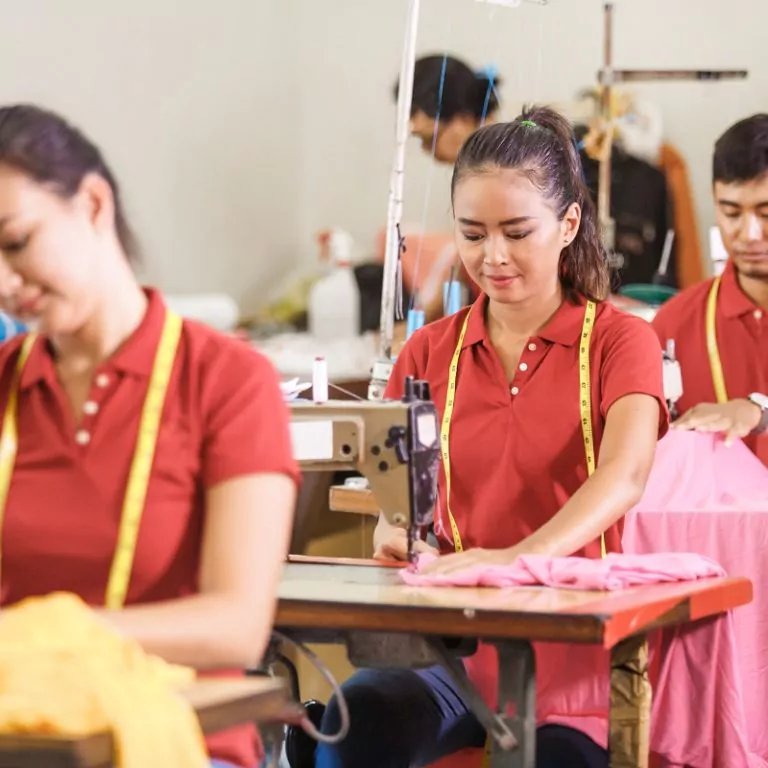 asian workers in garment factory sewing with industrial sewing m